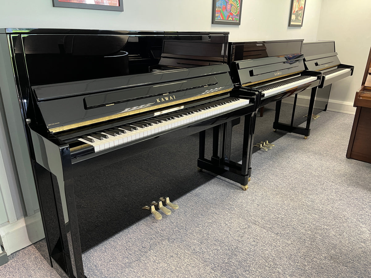 Chụp từ xa đàn piano KAWAI K15E đứng bên cạnh  cây đàn piano kawai khác để thấy rõ KAWAI K15E nhỏ bé hơn hẳn hai model còn lại