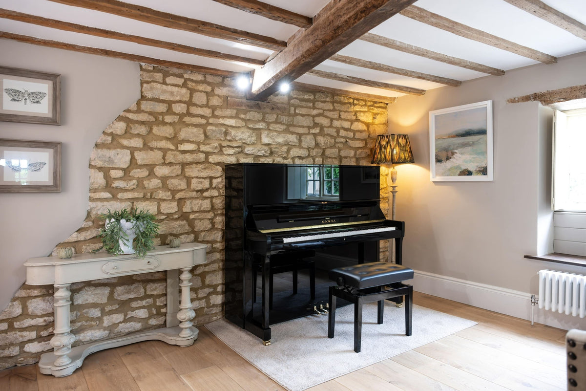 Toàn cảnh đàn piano KAWAI K600 chụp từ xa trong phòng khách sang trọng, đi kèm ghế, bên cạnh là bộ đèn trang trí kiểu quý tộc