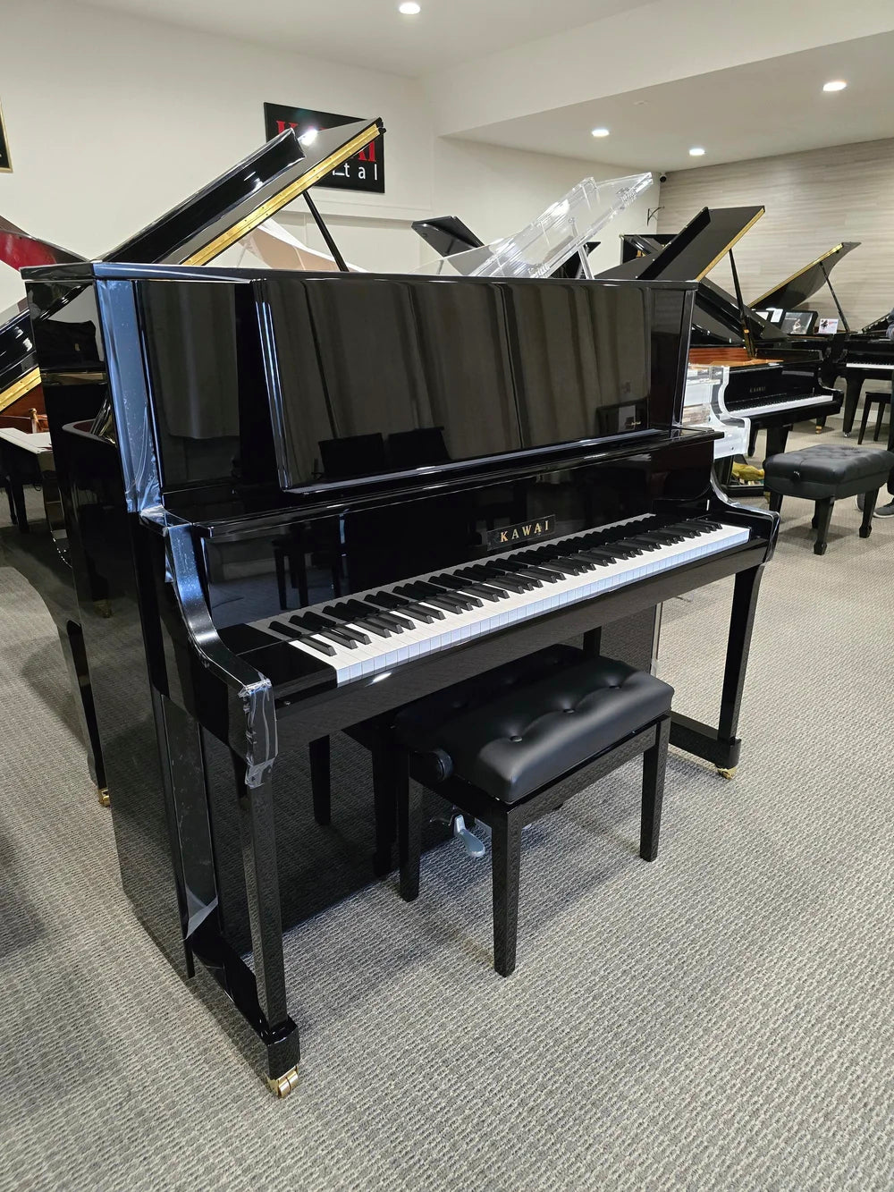Toàn cảnh đàn piano KAWAI K800 tại shworoom, nghiêng góc bên trái, cùng với ghế, xưng quanh là các cây grand piano