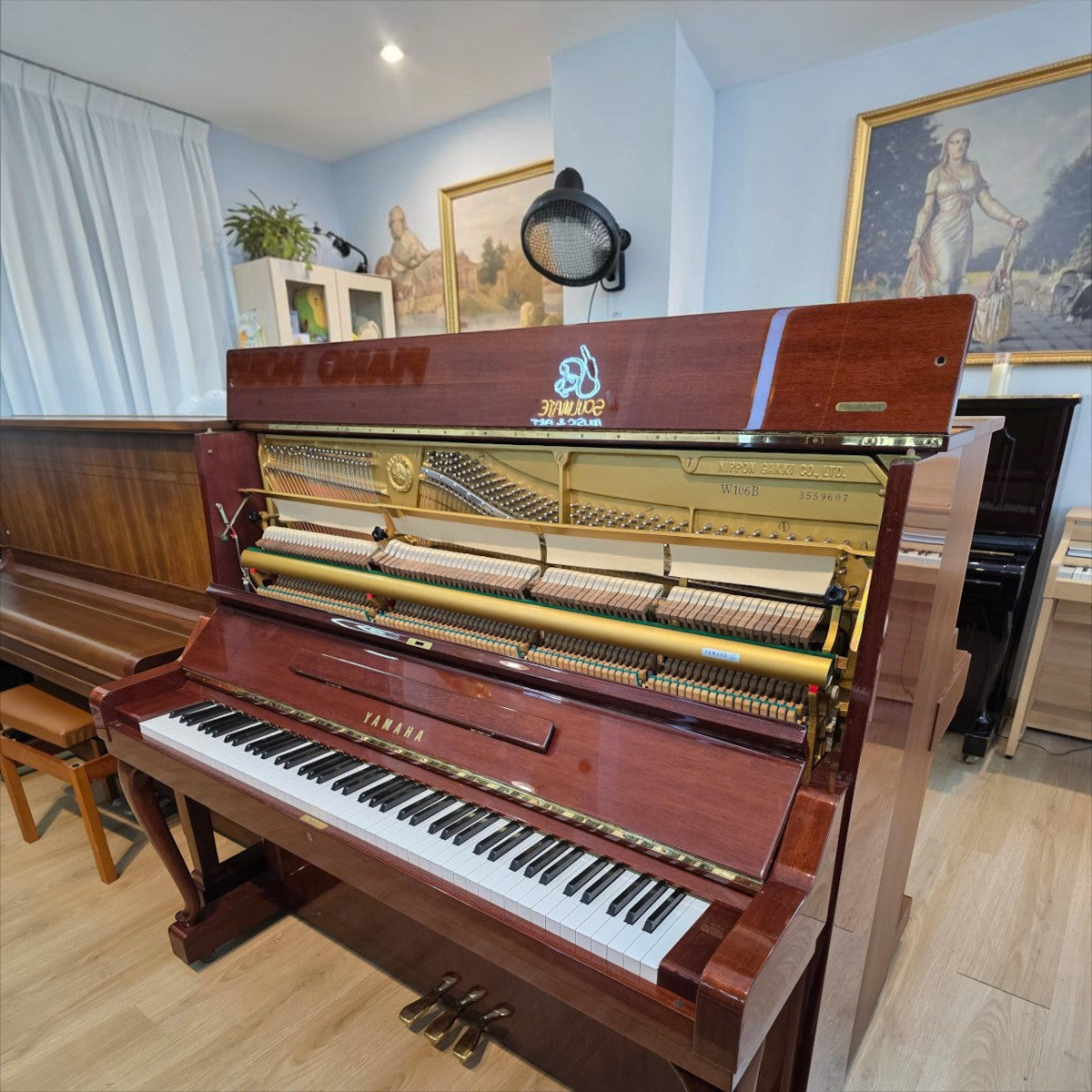 Đàn piano cơ Yamaha W106B tại TÂN NHẠC CỤ với lớp vỏ vân gỗ óc chó sang trọng, mở nắp để lộ bộ máy cơ bên trong.