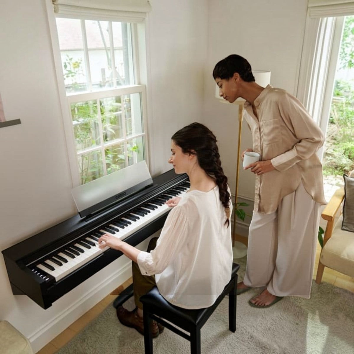 Người phụ nữ chơi đàn piano điện Casio AP-S200 màu đen tại Tân Nhạc Cụ, bên cạnh là người bạn đang đứng quan sát