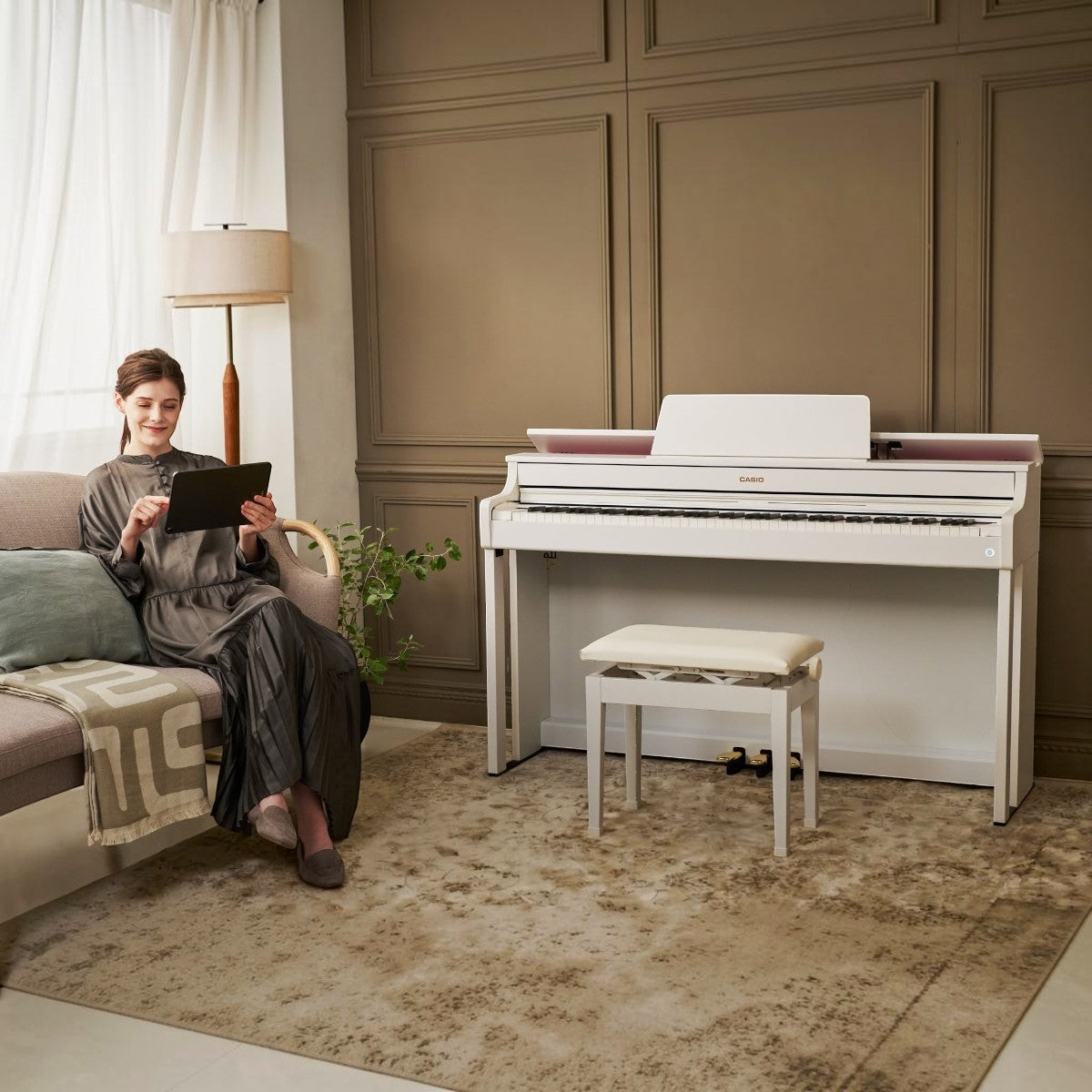 Người phụ nữ sử dụng máy tính bảng bên cạnh đàn piano điện Casio AP-300 màu trắng sang trọng tại TÂN NHẠC CỤ