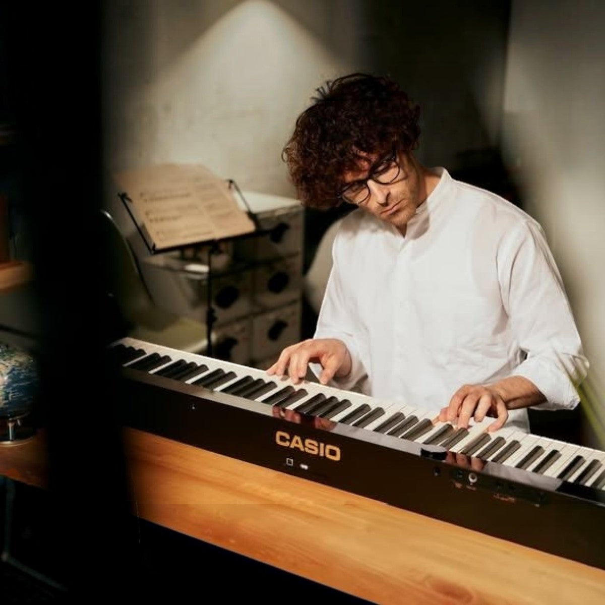 Nam nghệ sĩ đeo kính đang chơi đàn piano điện Casio PX-S5000 tại showroom TÂN NHẠC CỤ, cận cảnh phím gỗ vân sam.