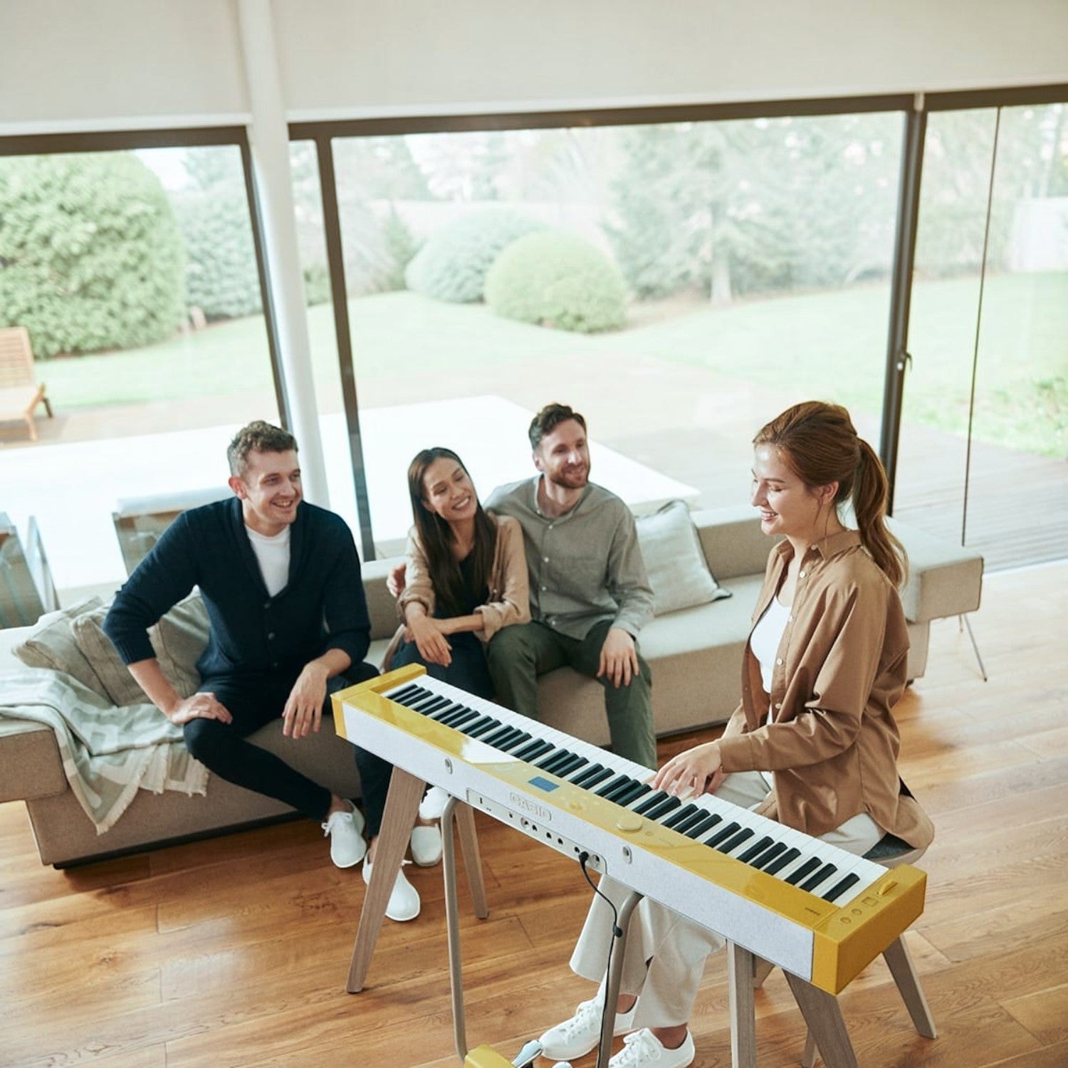 Người phụ nữ chơi đàn piano điện Casio PX-S7000 màu vàng Harmonious Mustard tại TÂN NHẠC CỤ, cùng bạn bè trong phòng khách