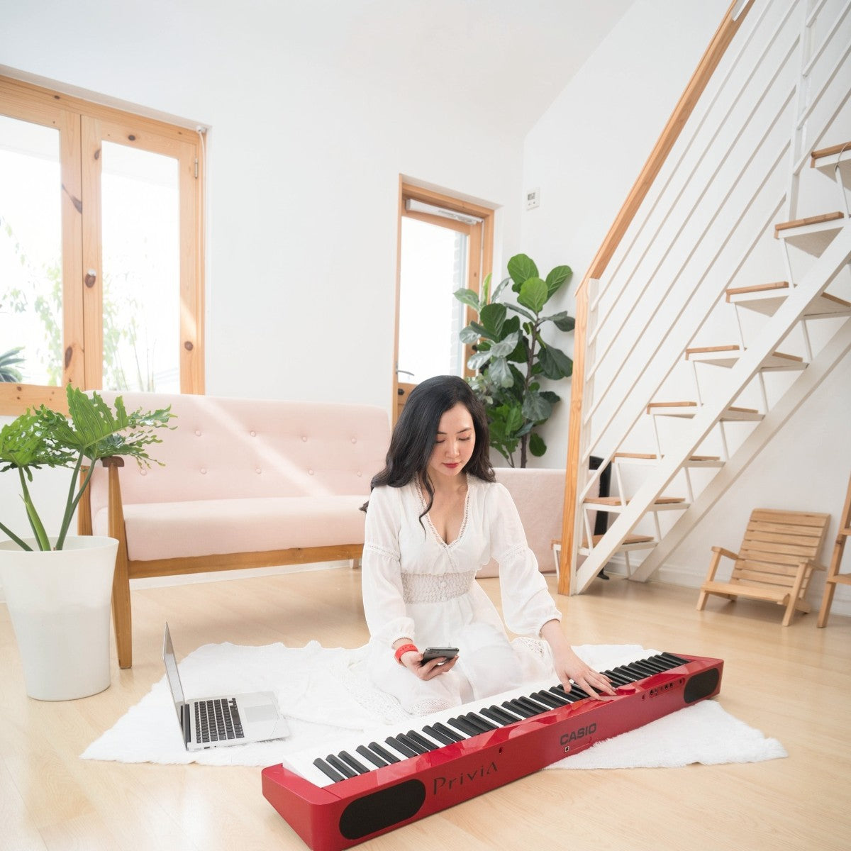 Người phụ nữ mặc váy trắng chơi đàn piano điện Casio PX-S1000 màu đỏ tại TÂN NHẠC CỤ trong không gian phòng khách