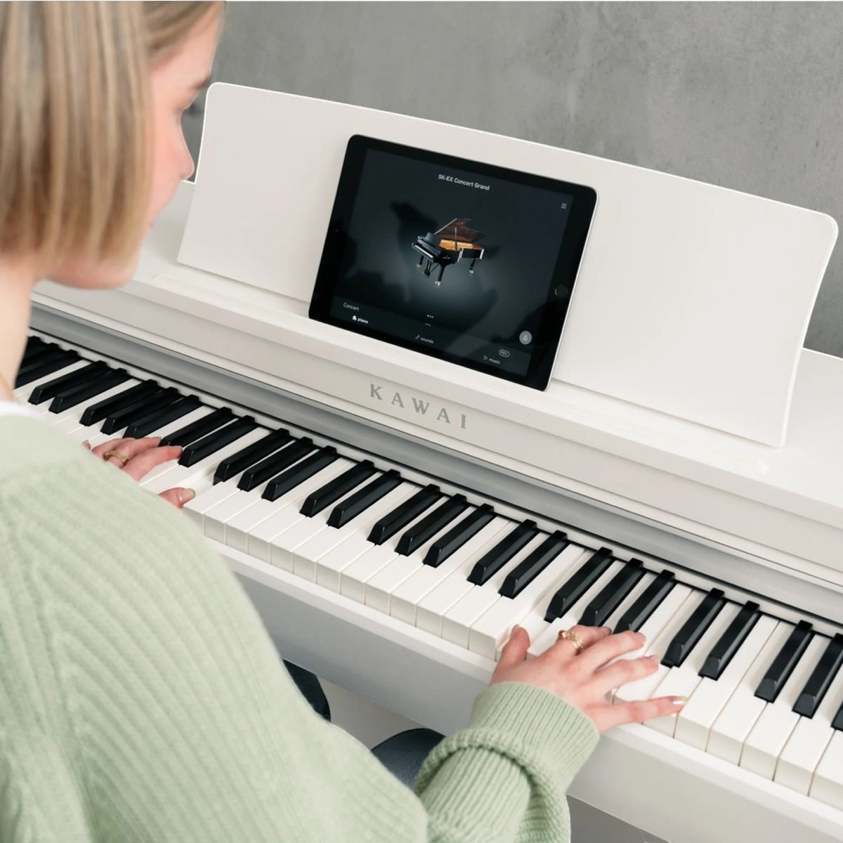 Người chơi đang sử dụng đàn piano điện Kawai CN201 màu trắng tại Tân Nhạc Cụ, kết nối máy tính bảng để học đàn