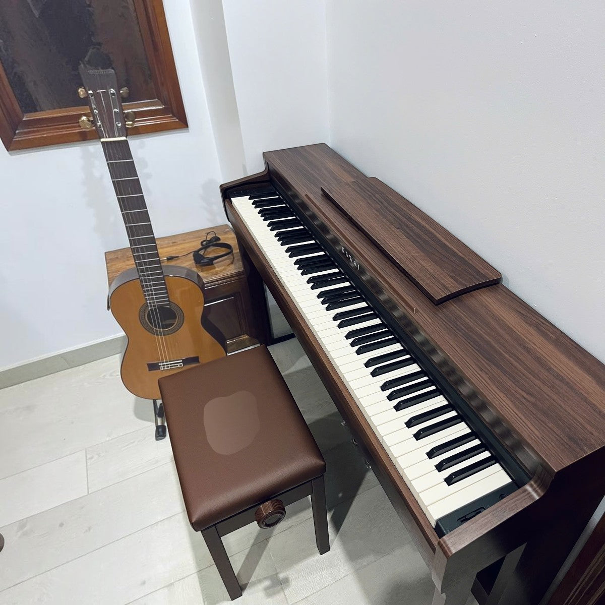 Đàn piano điện Kawai CN201 dáng tủ màu gỗ hồng sắc tại Tân Nhạc Cụ, kèm ghế và đàn guitar bên cạnh