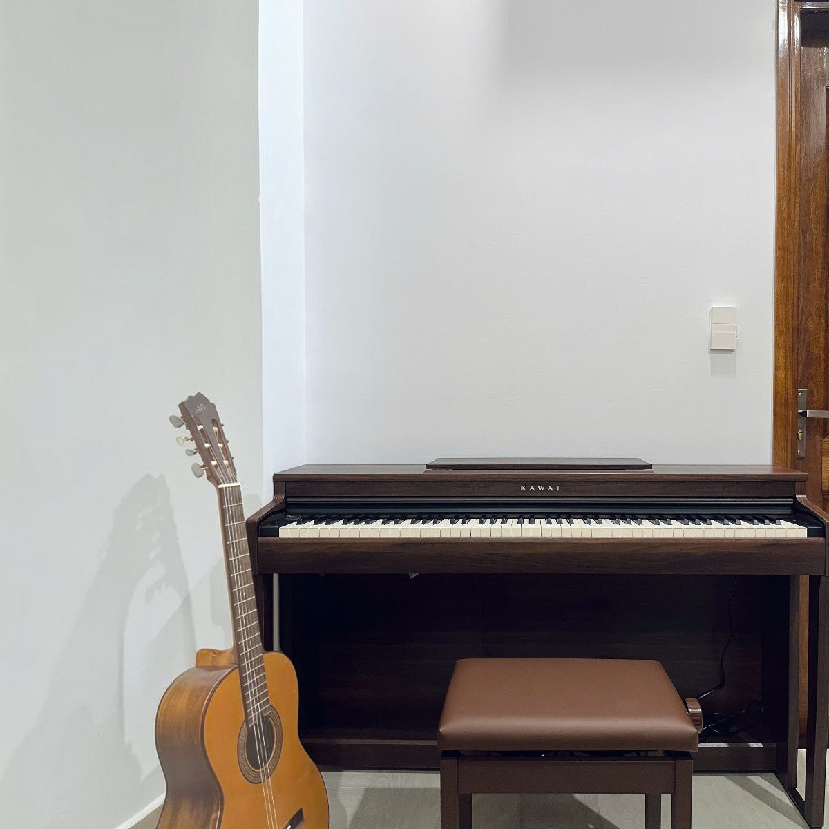 Đàn piano điện Kawai CN201 màu gỗ nâu tại TÂN NHẠC CỤ, thiết kế dáng tủ sang trọng với ghế đàn và đàn guitar bên cạnh