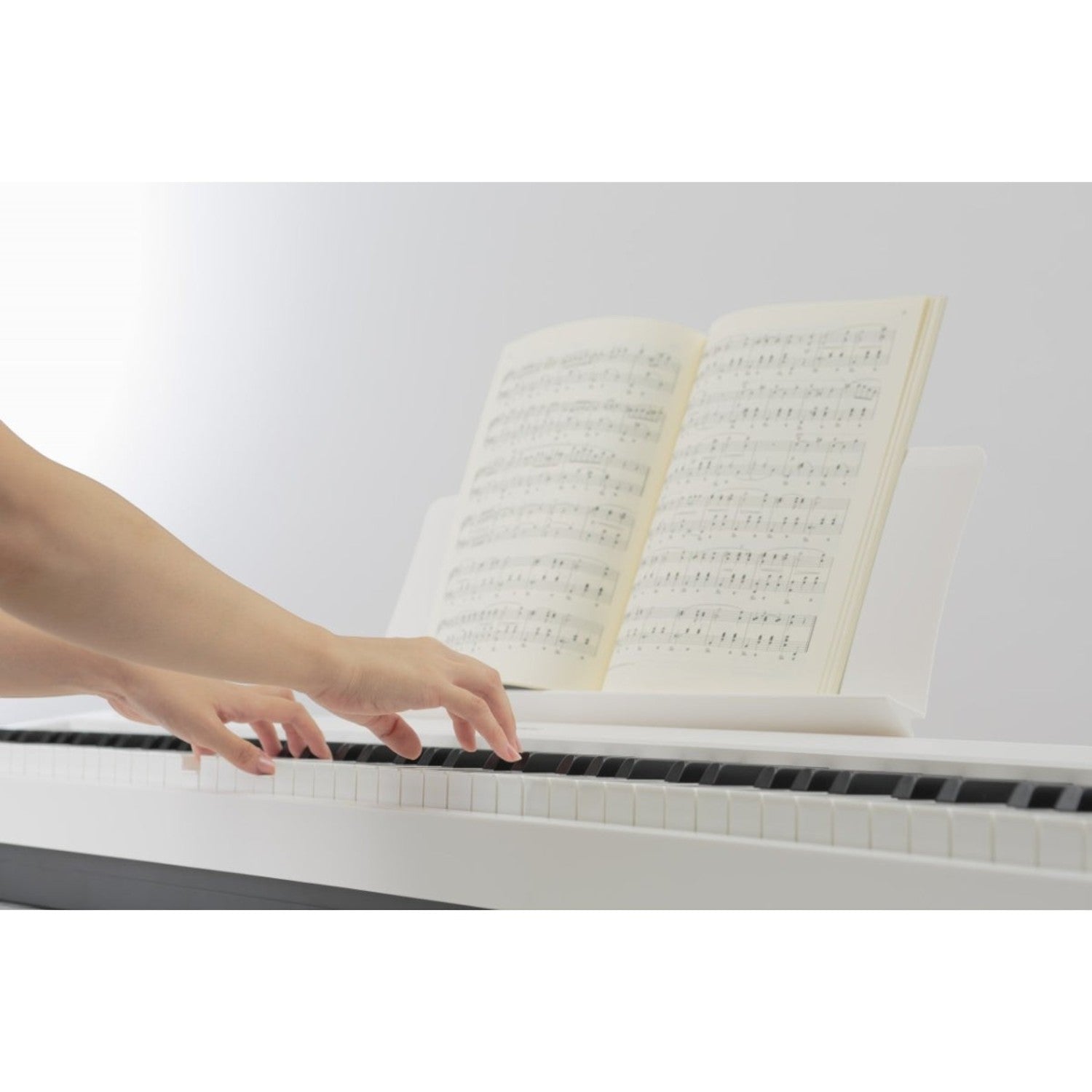 Người chơi đang tập luyện trên đàn piano điện Kawai ES110 màu trắng tại TÂN NHẠC CỤ với bản nhạc đặt trên giá đỡ