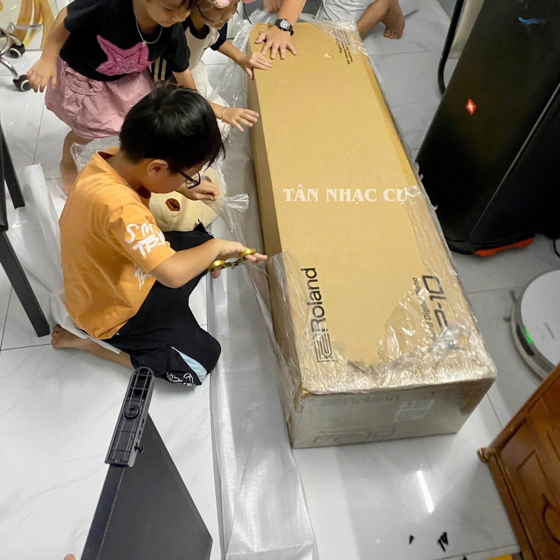 Trẻ em đang hào hứng mở hộp đàn piano điện Roland FP-10 mới tại Tân Nhạc Cụ