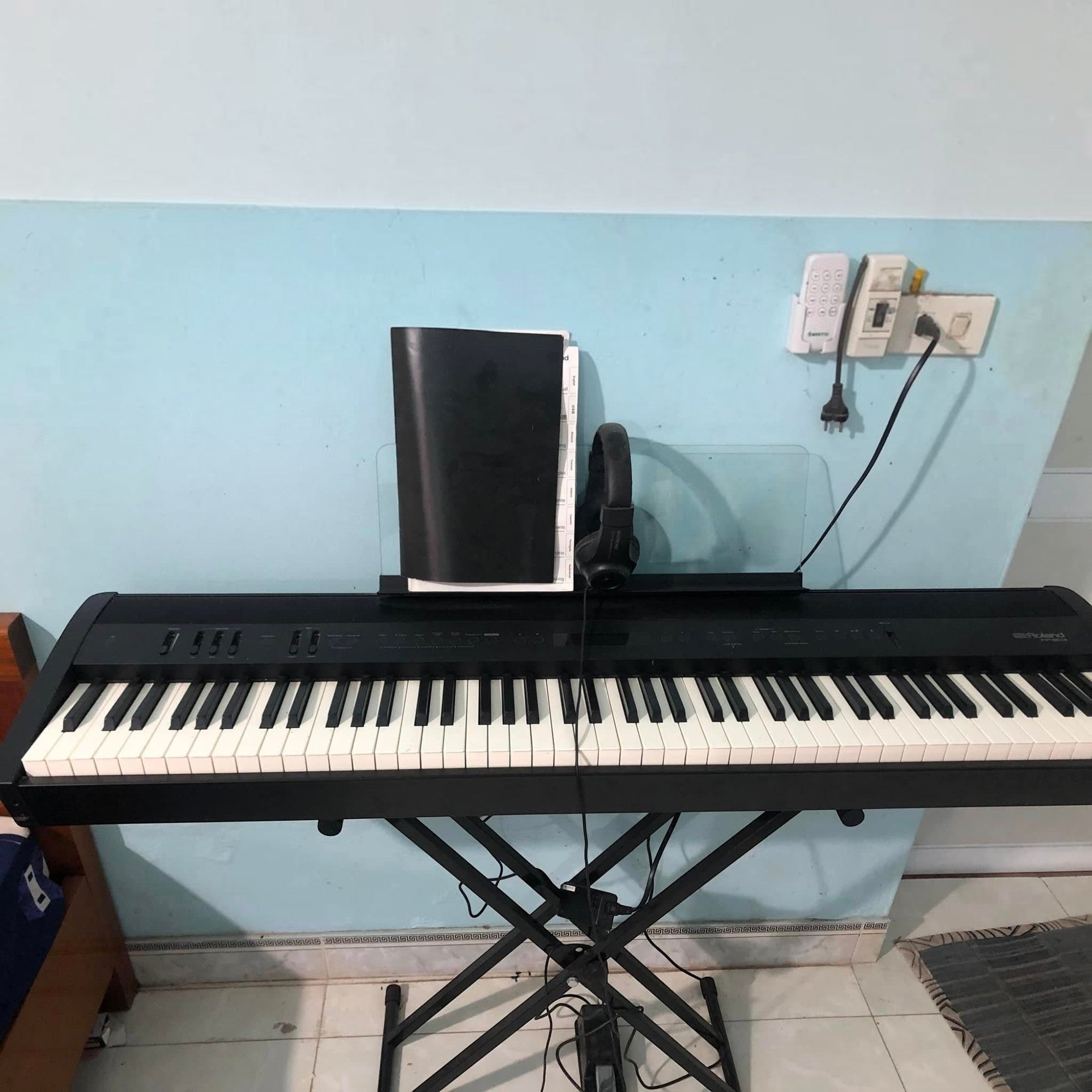 Đàn piano điện Roland FP-60X màu đen tại TÂN NHẠC CỤ, đặt trên chân đế X với tai nghe và giá nhạc