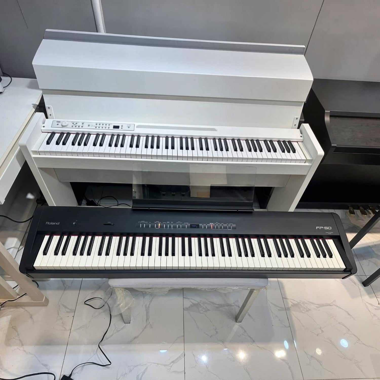 Đàn piano điện Roland FP-E50 màu đen đặt phía trước một cây đàn piano điện màu trắng tại showroom TÂN NHẠC CỤ
