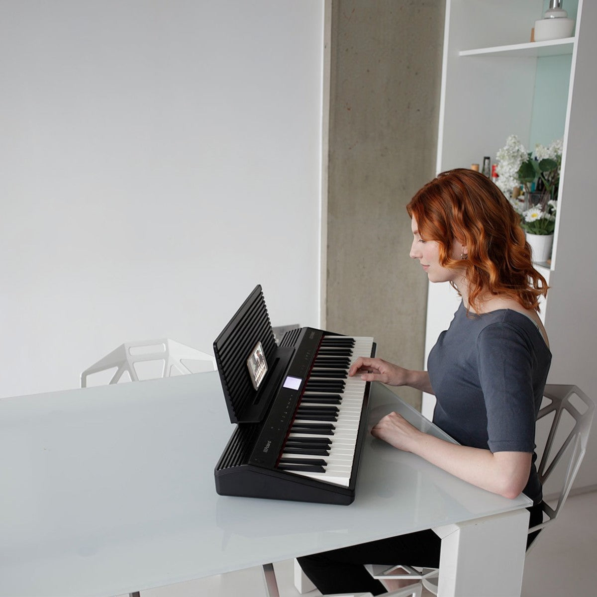 Cô gái tóc đỏ chơi đàn piano điện Roland GO:61 màu đen tại bàn ăn trong không gian hiện đại của Tân Nhạc Cụ