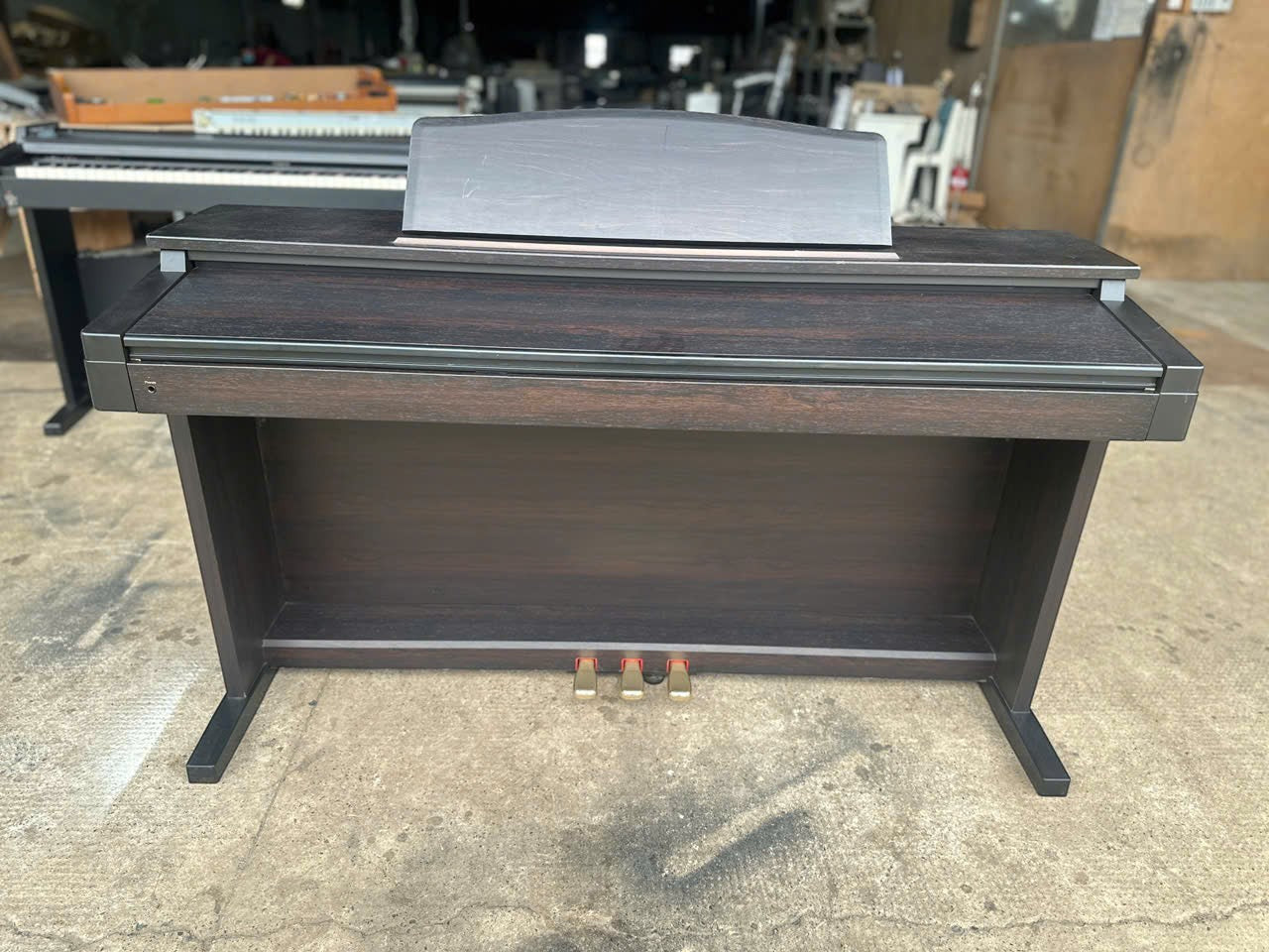 Đàn piano điện Roland HP230R từ Tân Nhạc Cụ với thiết kế gỗ màu nâu đậm sang trọng và ba pedal chắc chắn