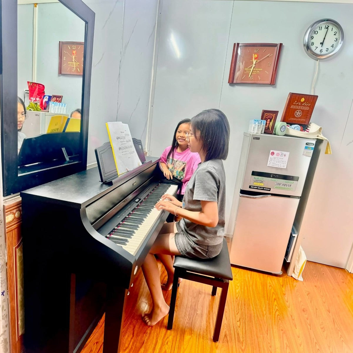 Cô bé đang chơi đàn piano điện Roland HP508GP màu đen bóng gương tại TÂN NHẠC CỤ, có em nhỏ ngồi cạnh quan sát