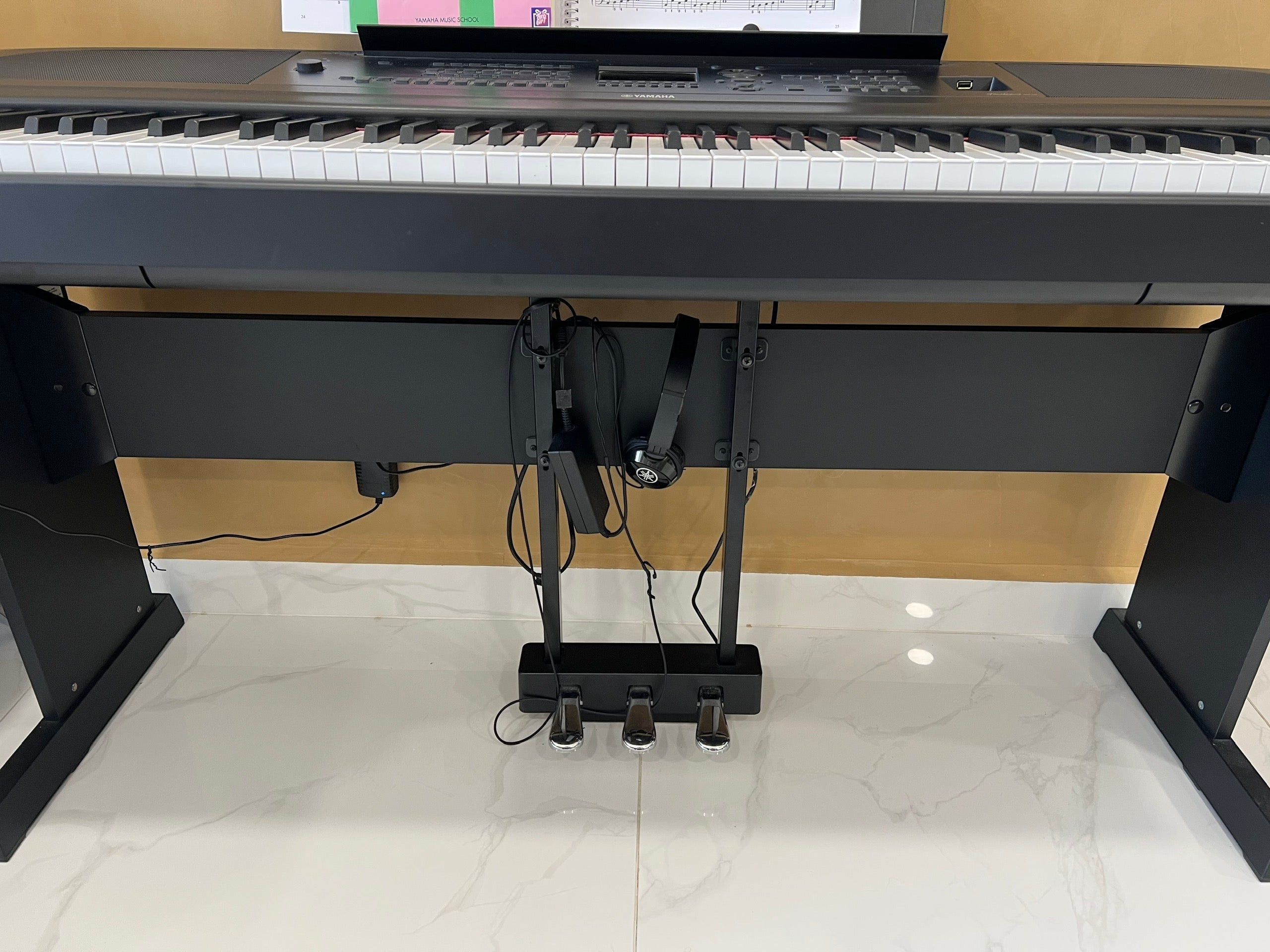 Đàn piano điện TÂN NHẠC CỤ Yamaha DGX670 màu đen với bộ ba pedal và tai nghe gắn phía dưới chân đàn
