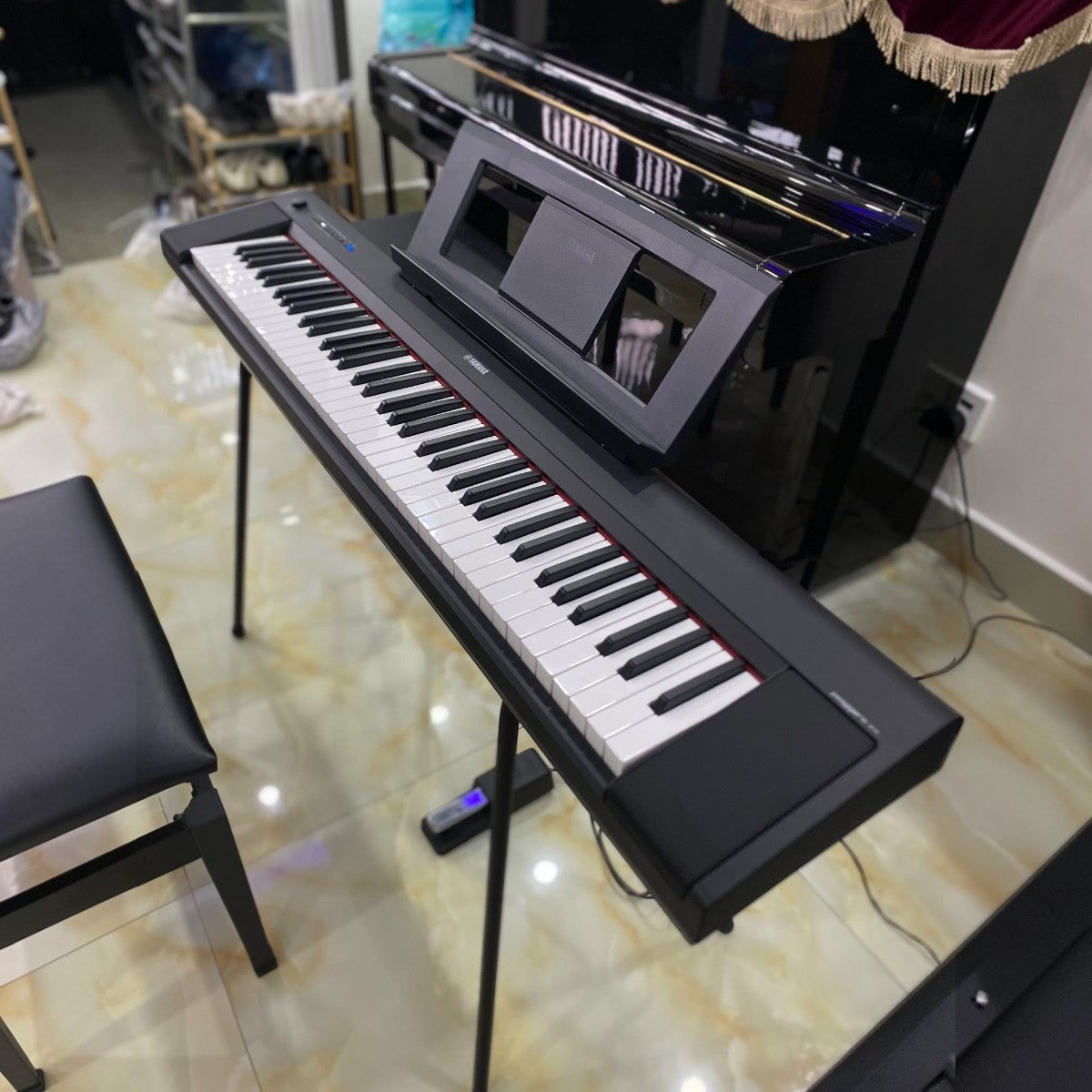 Đàn piano điện TÂN NHẠC CỤ Yamaha NP35 màu đen với 76 phím, thiết kế gọn nhẹ, đặt trên chân đàn tại showroom