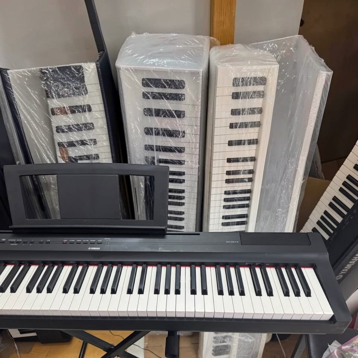 Đàn piano điện Yamaha P125 màu đen tại showroom TÂN NHẠC CỤ, phía sau là các cây đàn được bọc bảo vệ cẩn thận
