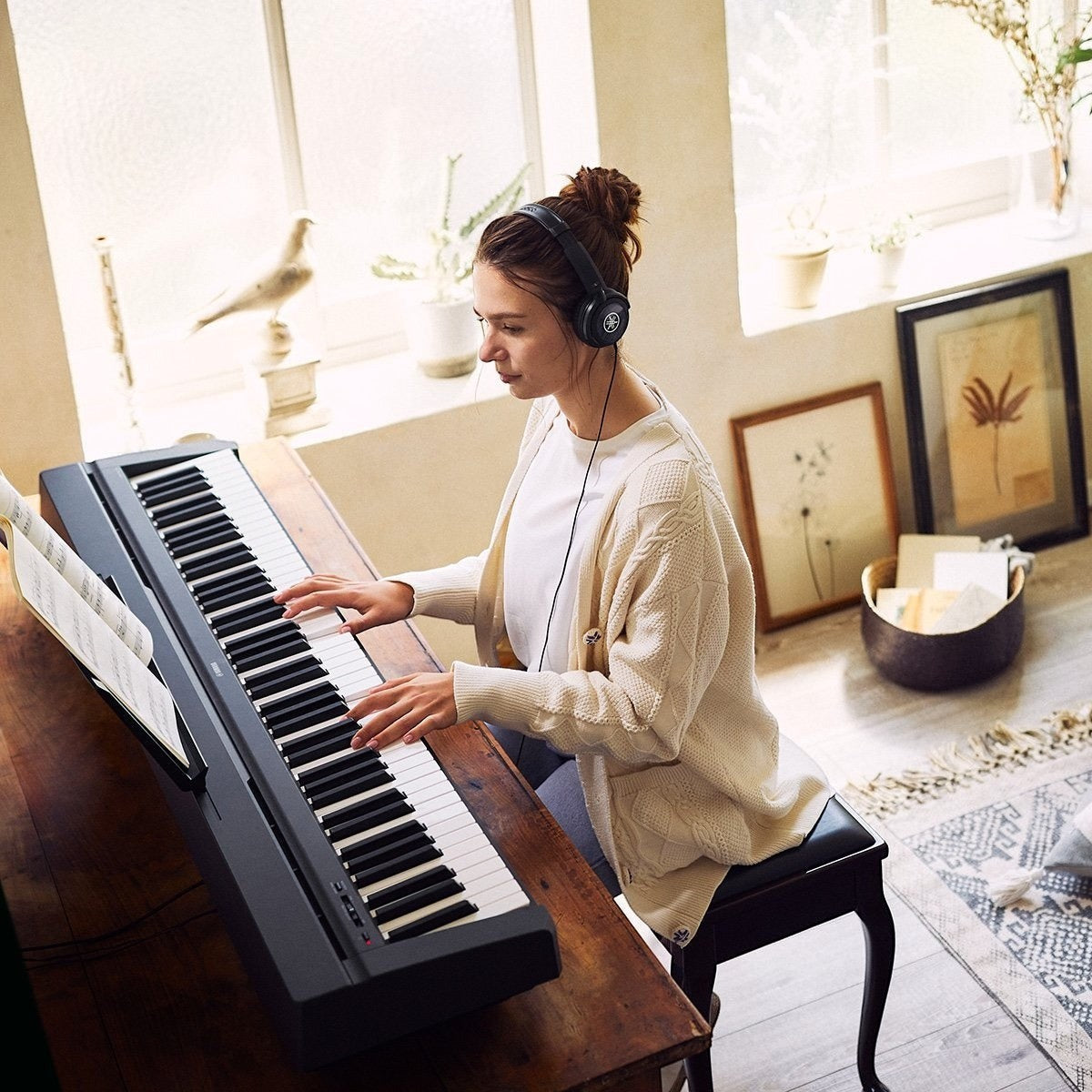 Cô gái đeo tai nghe chơi đàn piano điện Yamaha P45 cũ màu đen trong không gian phòng khách ấm cúng tại Tân Nhạc Cụ