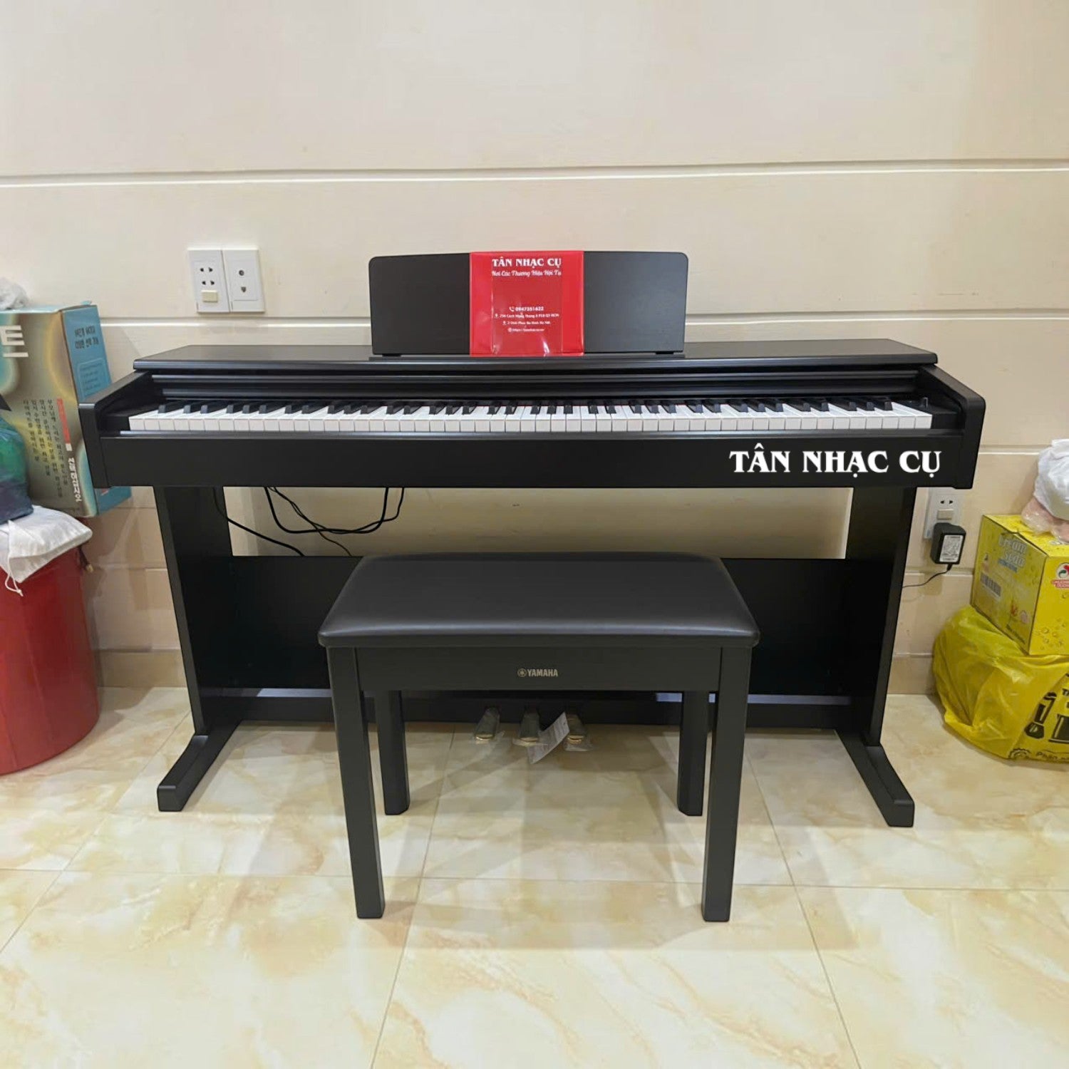 Đàn piano điện Yamaha YDP-105 màu đen tại TÂN NHẠC CỤ, thiết kế dáng tủ đứng kèm ghế ngồi và giá nhạc.