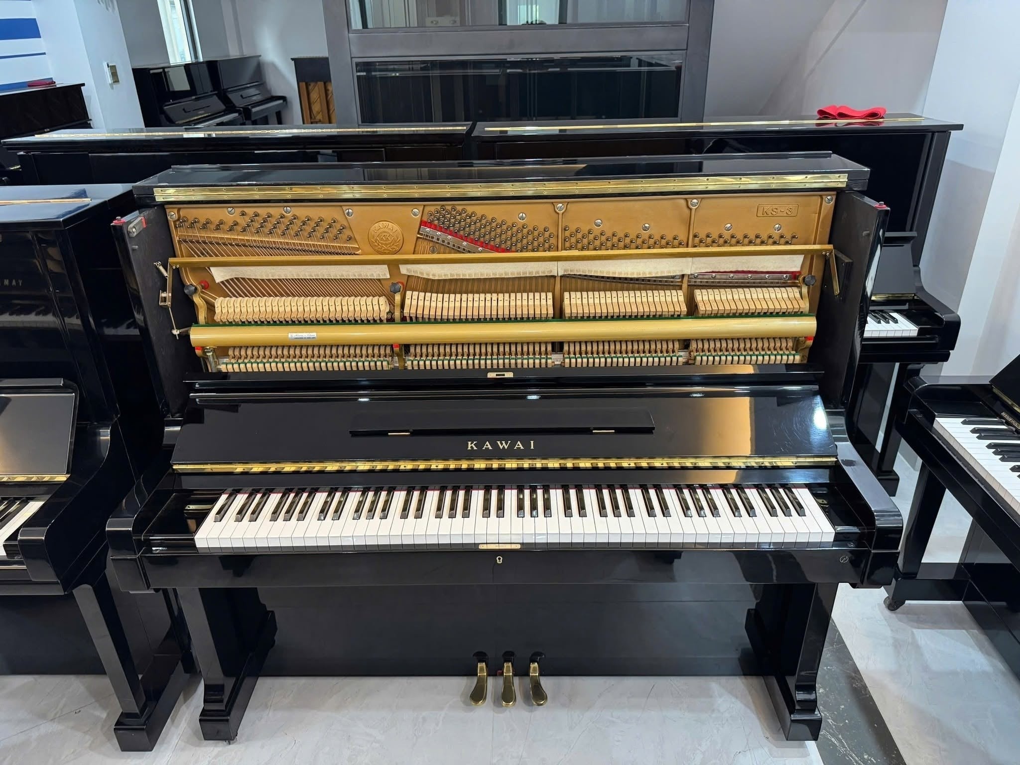 Đàn piano cơ upright Kawai KS3 màu đen bóng tại Tân Nhạc Cụ, lộ bộ máy cơ bên trong với khung gang vàng sang trọng