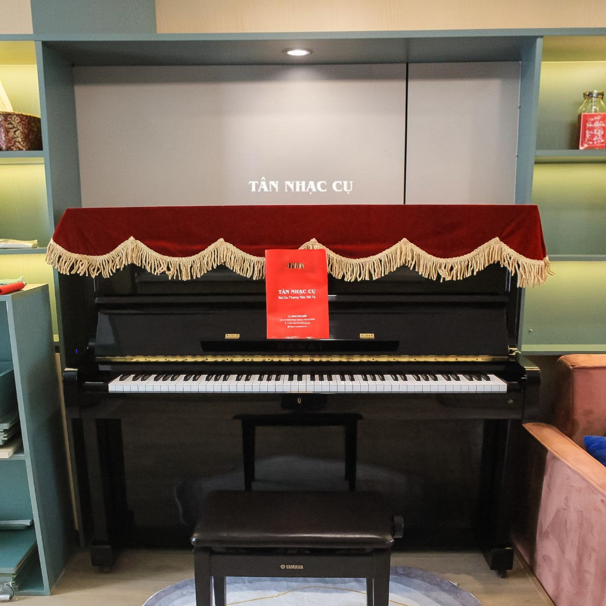 Đàn piano cơ upright Kawai KS3F màu đen bóng sang trọng tại TÂN NHẠC CỤ với khăn phủ đỏ viền tua rua cổ điển