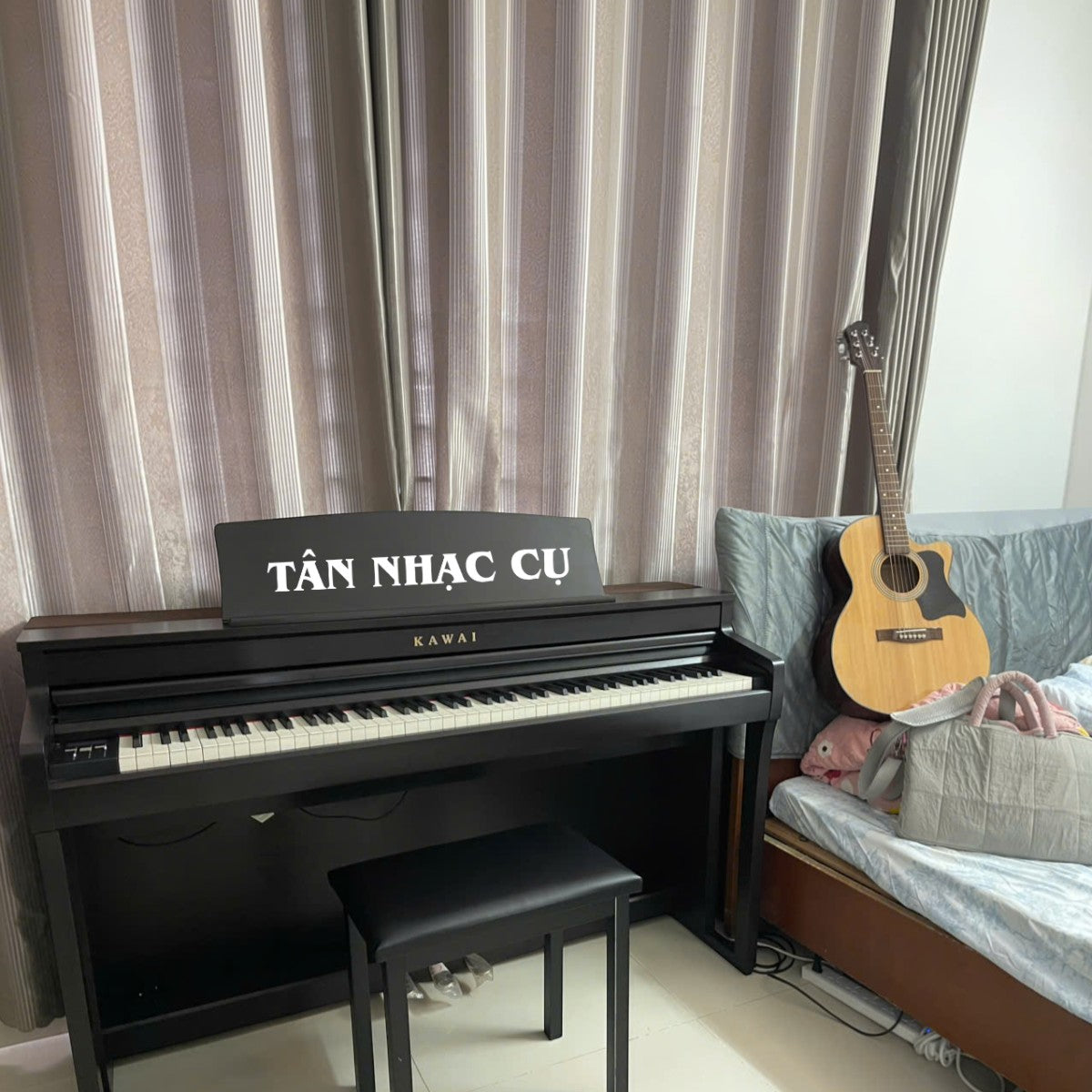 Đàn piano điện TÂN NHẠC CỤ Kawai CA59 màu đen với phím gỗ, đặt cạnh đàn guitar trong phòng ngủ.