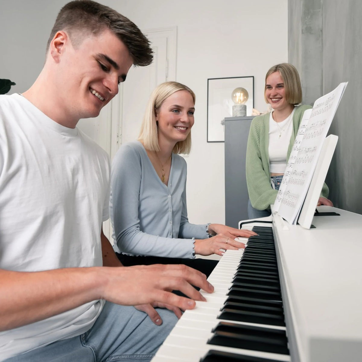 Ba người trẻ vui vẻ chơi đàn piano điện Kawai CN201 màu trắng satin tại TÂN NHẠC CỤ trong không gian gia đình ấm cúng