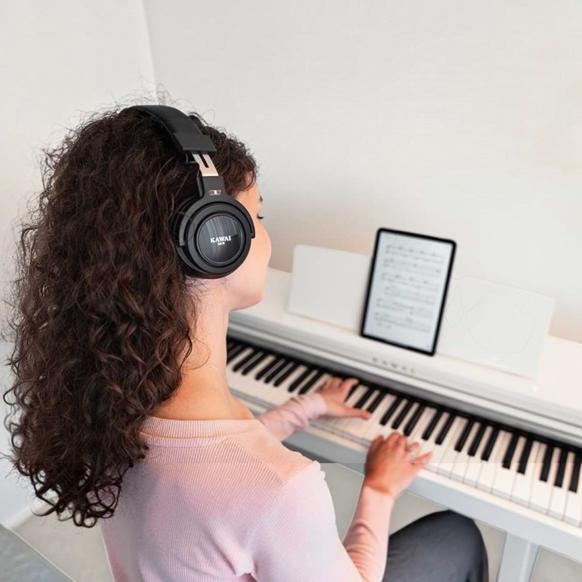 Người chơi đàn piano điện Kawai CX102 màu trắng, đeo tai nghe Kawai, tập luyện với máy tính bảng tại Tân Nhạc Cụ