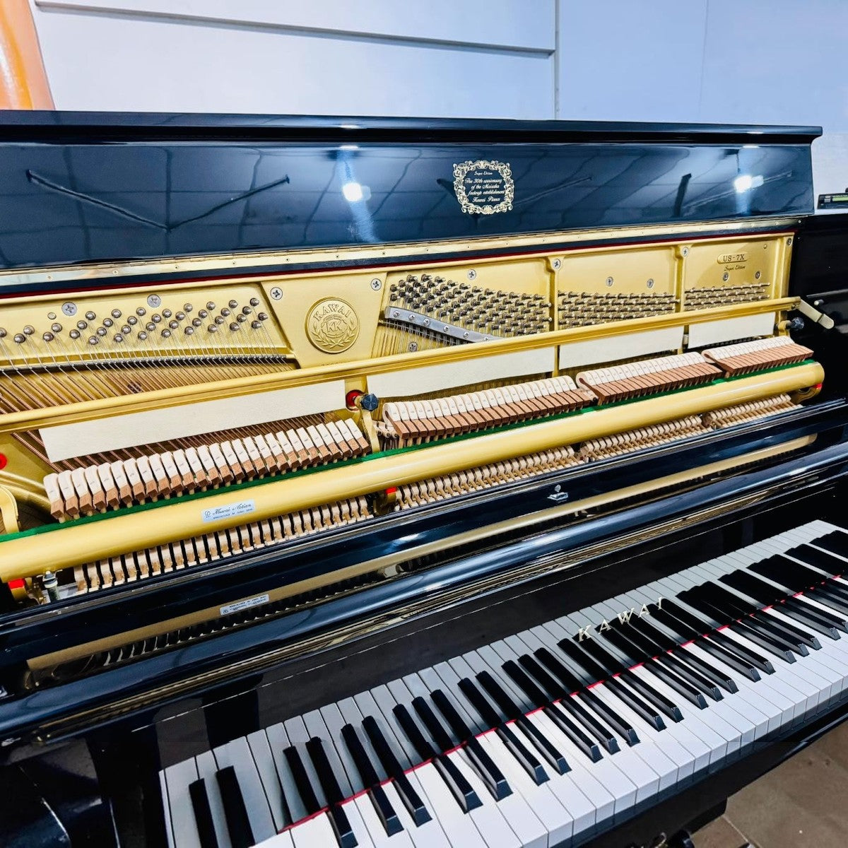 Đàn piano cơ upright Kawai US7X màu đen bóng tại TÂN NHẠC CỤ, lộ bộ máy bên trong với khung gang vàng sang trọng.