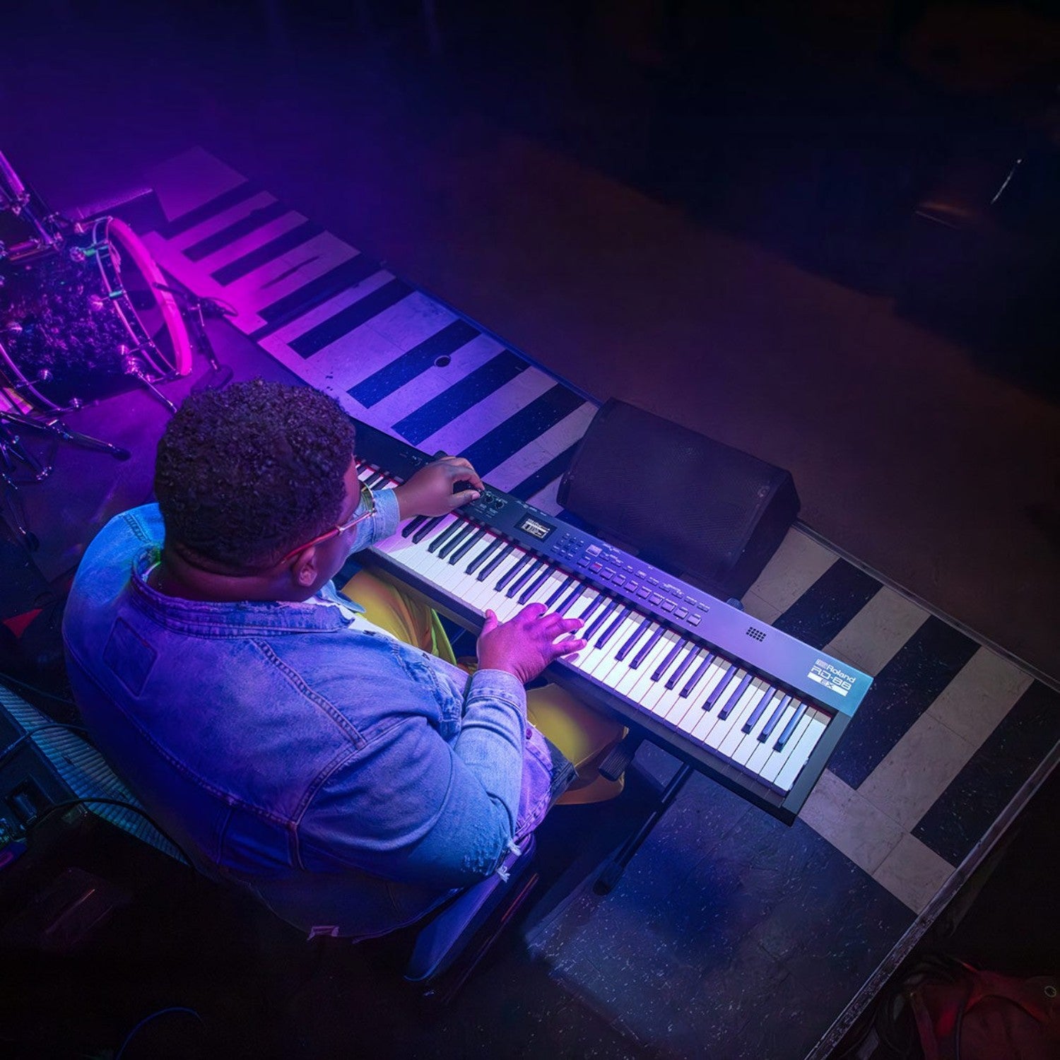 Nhạc sĩ biểu diễn đàn piano điện Roland RD-88 EX trên sân khấu với ánh sáng tím, góc nhìn từ trên cao
