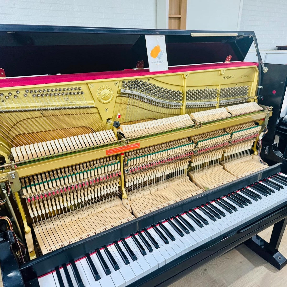Đàn piano cơ TÂN NHẠC CỤ Yamaha HQ300SX màu đen bóng, lộ bộ máy cơ bên trong với khung gang vàng và búa đàn chi tiết.