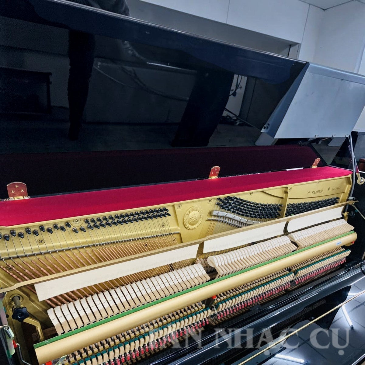Đàn piano cơ Yamaha SX100RBL màu đen bóng tại TÂN NHẠC CỤ, lộ bộ cơ và khung gang vàng bên trong